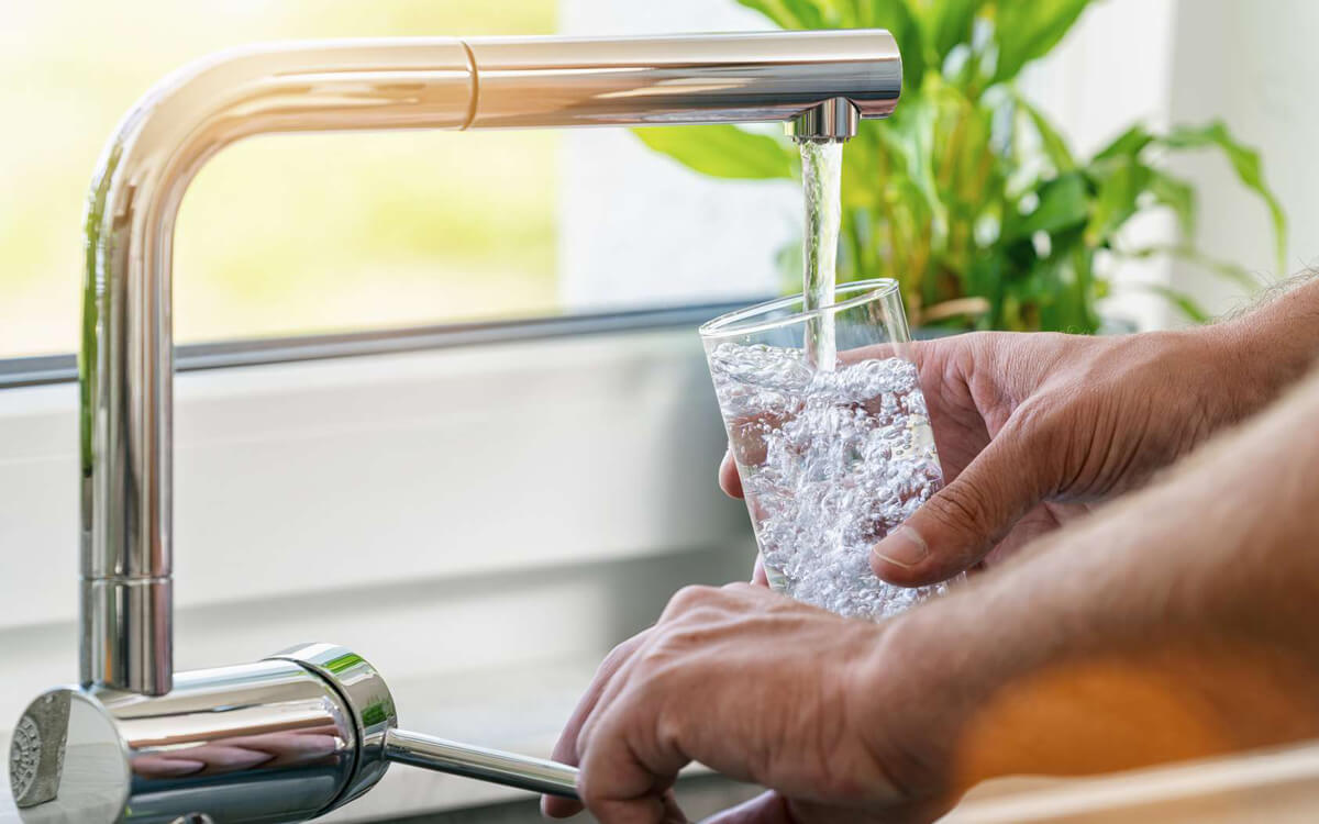 homme qui se sert un verre d'eau au robinet